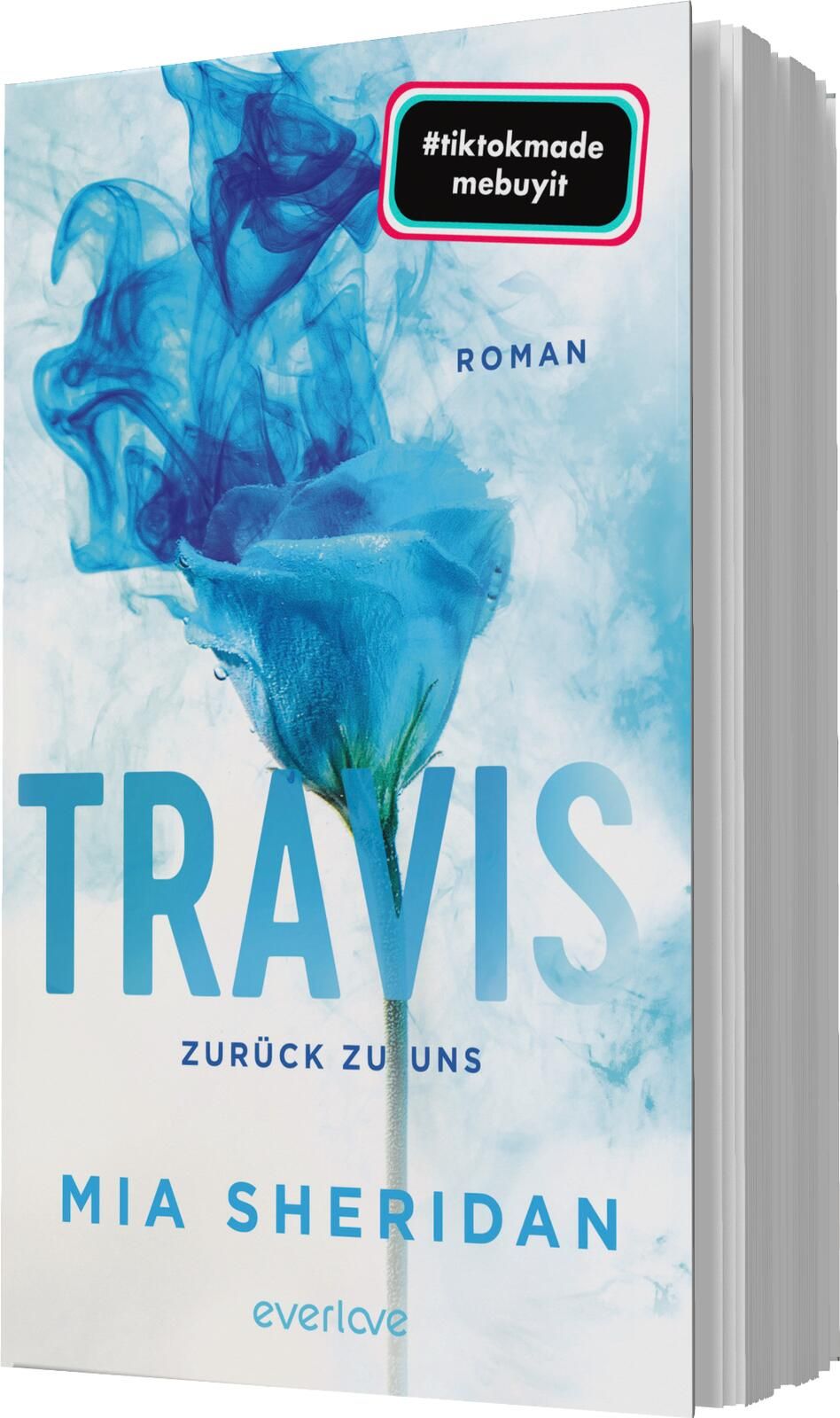 Das Buchcover zeigt einen sanften, hellblauen Hintergrund mit einem geschwungenen Rauchmuster, das eine mystische Atmosphäre erzeugt. Im Vordergrund befindet sich eine blaue Rose mit grünen Blättern. Der Titel „TRAVIS“ ist in großen, auffälligen Buchstabe