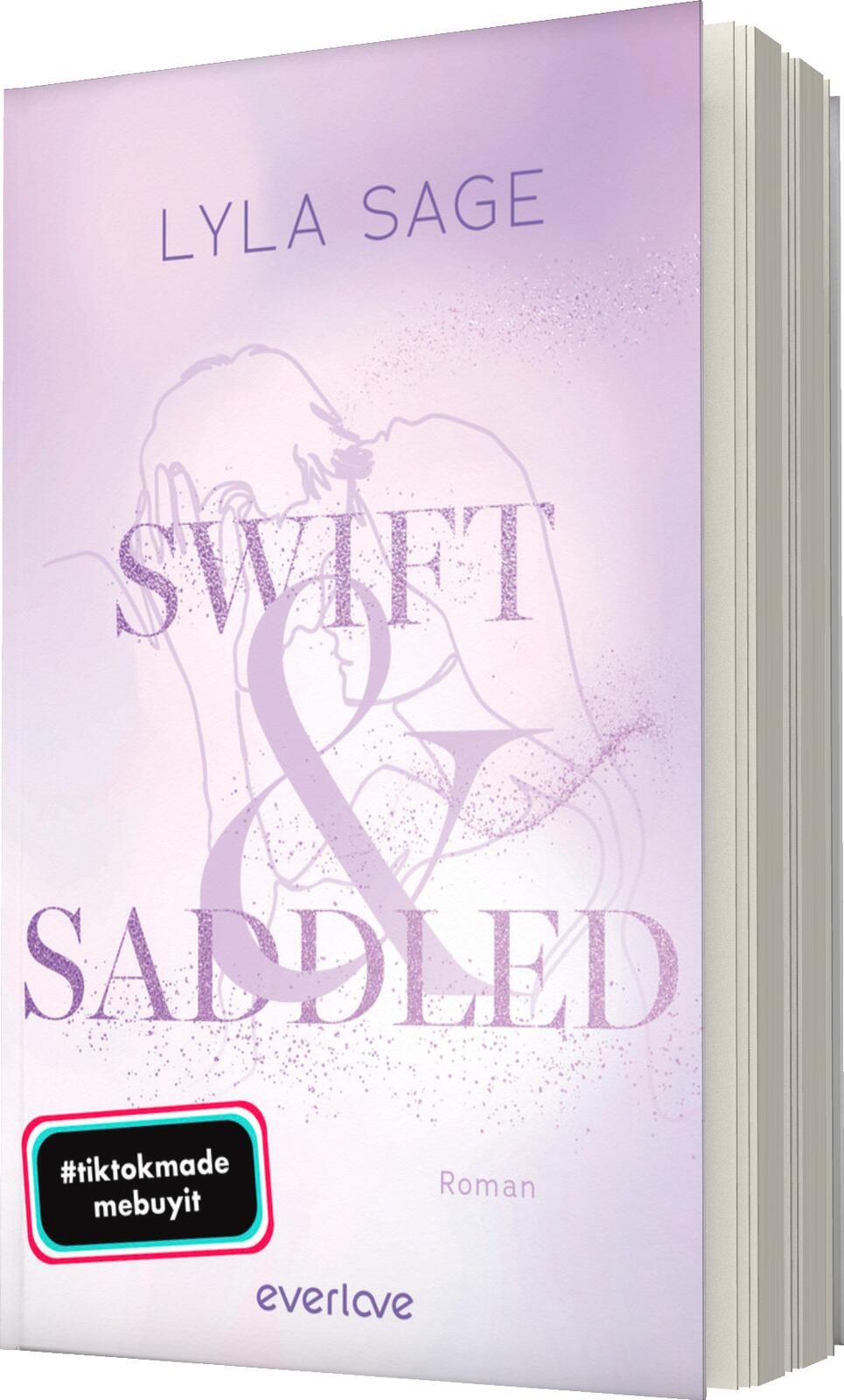 Das Buchcover zeigt einen sanften lilafarbenen Hintergrund mit einem verschwommenen, romantischen Paar im oberen Bereich. Der Titel „SWIFT & SADDLED“ ist in großer, geschwungener Schrift in einem leicht glitzernden Rosa platziert, wobei das Wort „&“ beson